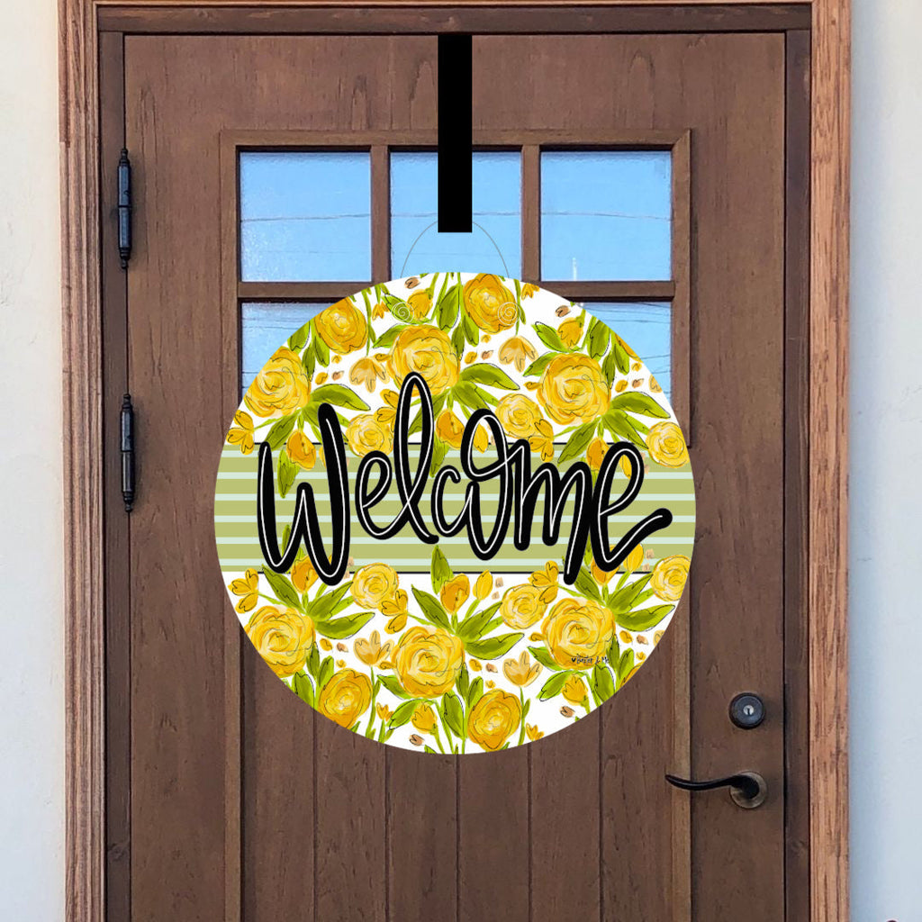Round decorative door sign with yellow floral pattern and 'Welcome' text on a wooden door.