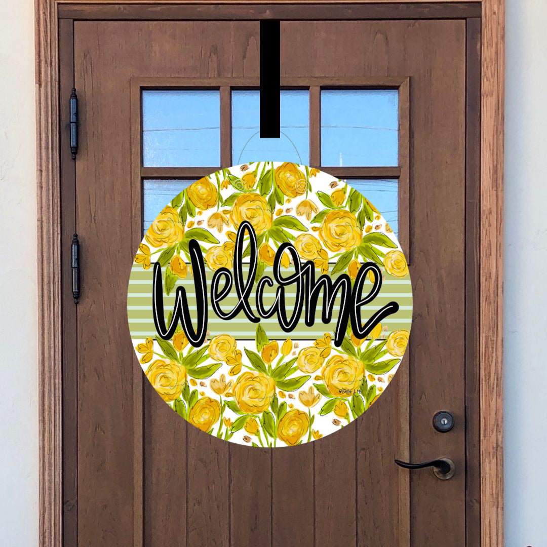 Round decorative door sign with yellow floral pattern and 'Welcome' text on a wooden door.